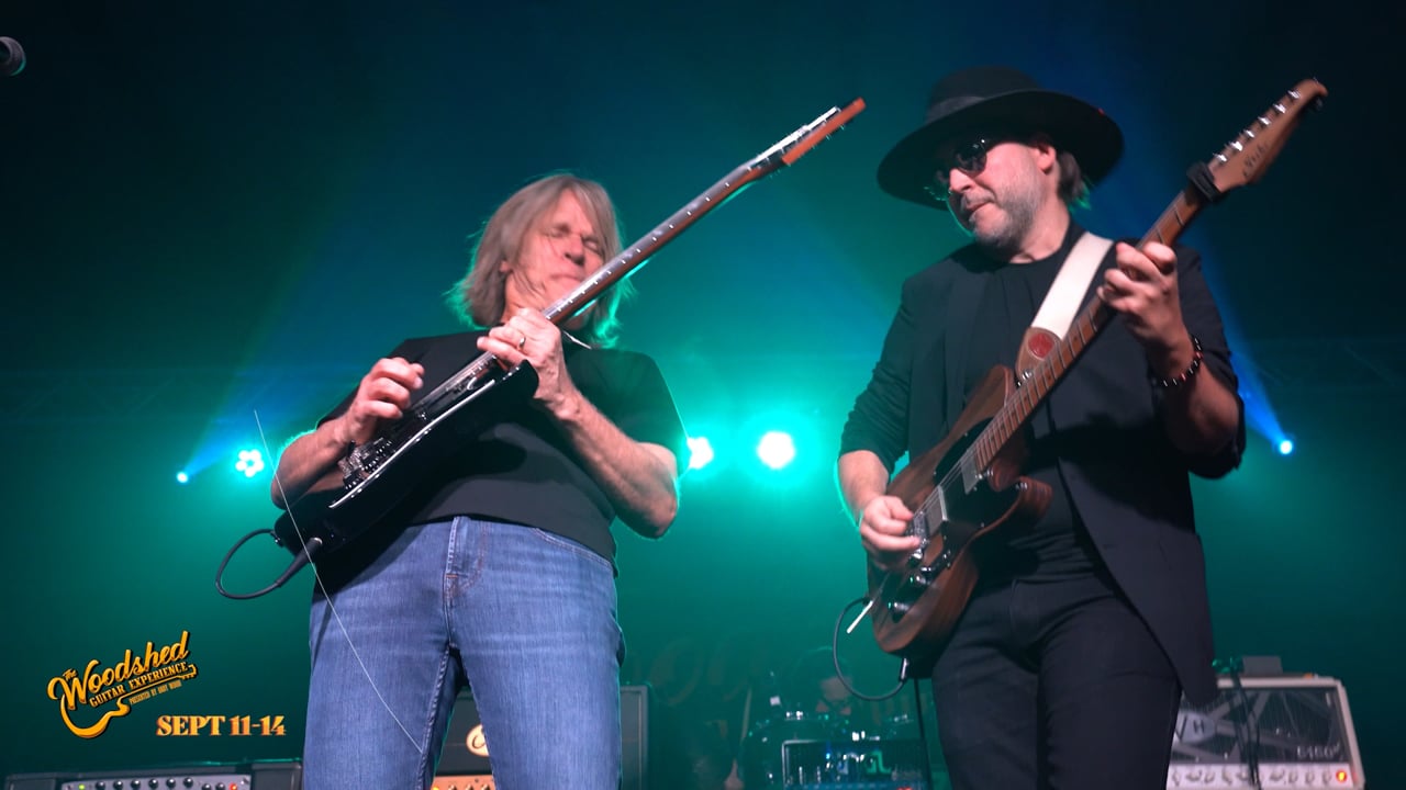 Two guitarists trading solos under stage lights at the Woodshed Guitar Experience